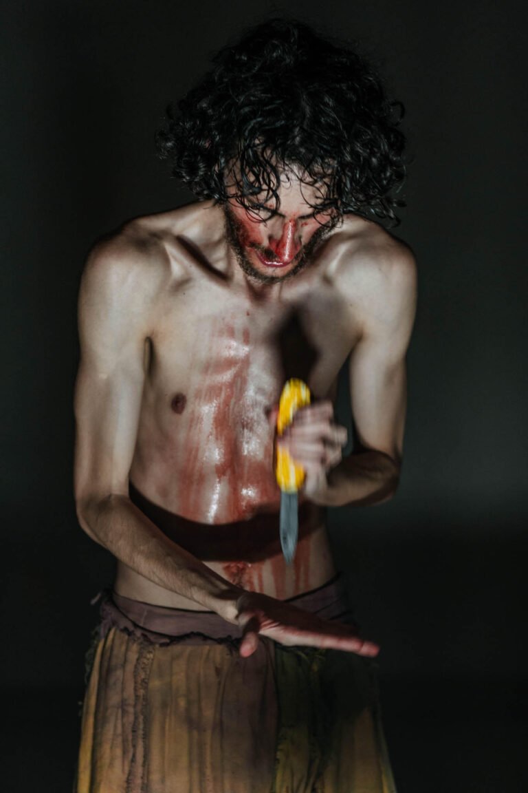 Yuri Fidelis em cena de CUME, corpo manchado de sangue segurando uma faca