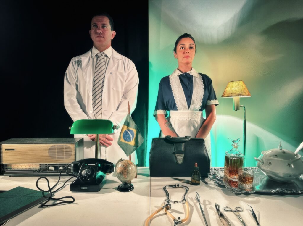 Pedro Osório e Maíra Chasseraux em cena de Dr. Carrasco e sua criada Matti, divididos entre consultório e cozinha