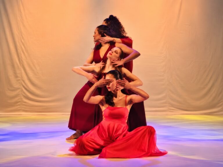 Grupo de bailarinas em vestidos vermelhos em pose escultórica, cena de O Tempo das Coisas