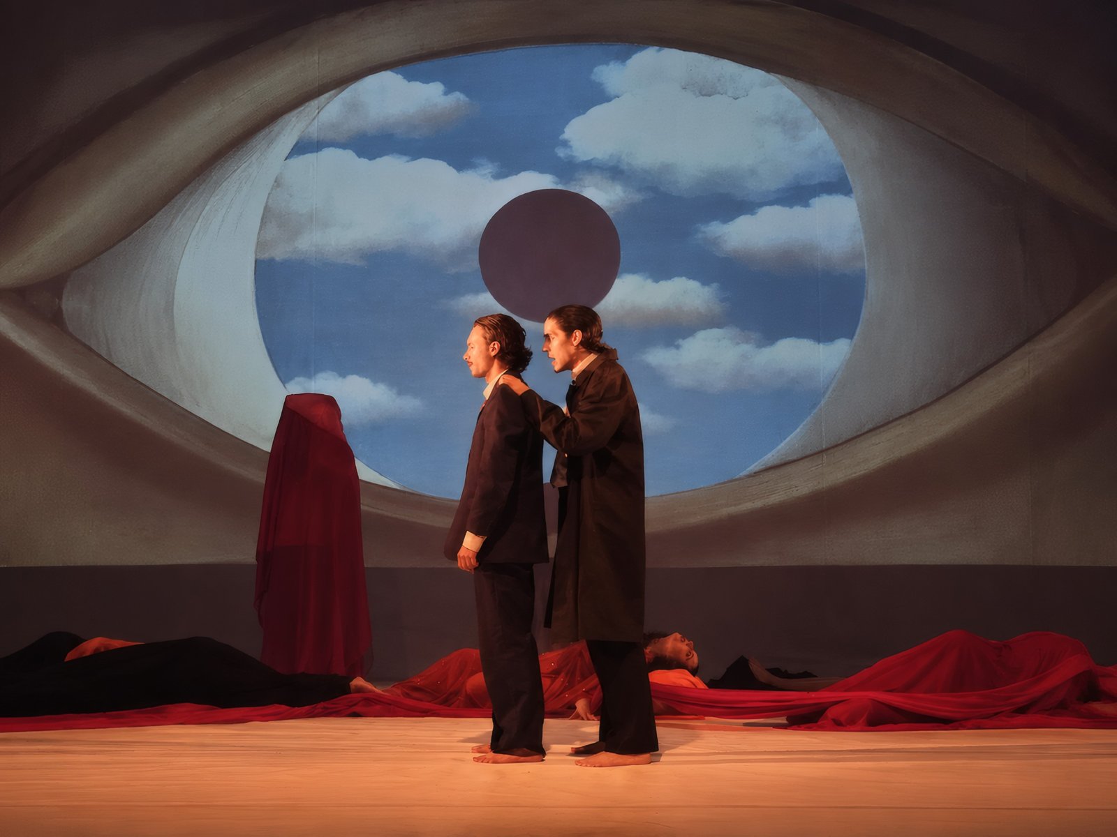 Dois atores em cena diante de um cenário em formato de olho com céu e nuvens, referência a Magritte