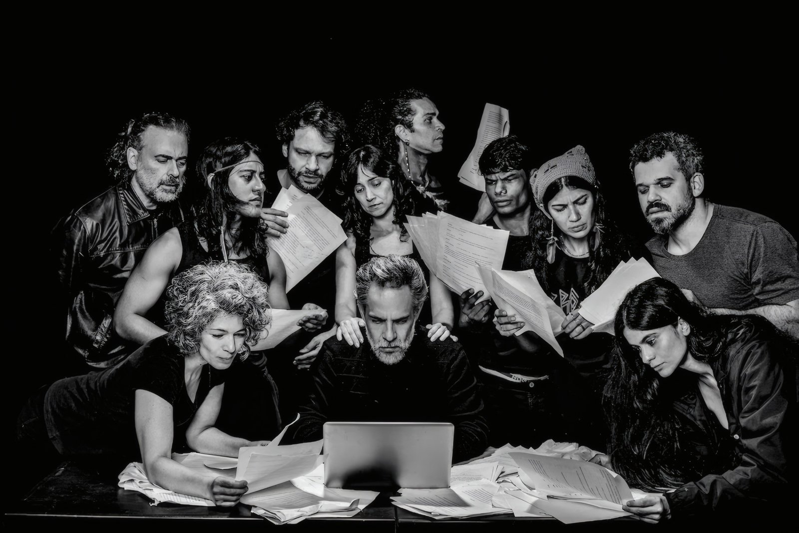 Elenco de Quase uma Estória reunido ao redor de uma mesa lendo textos, em preto e branco