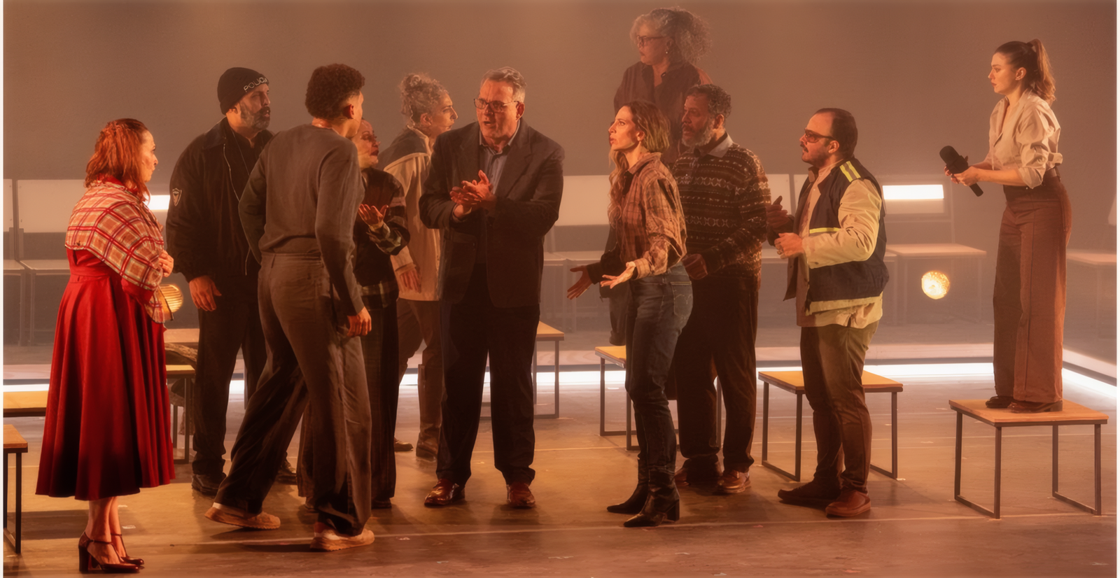 Cena de Vindos de Longe com o elenco reunido no palco em torno de mesas